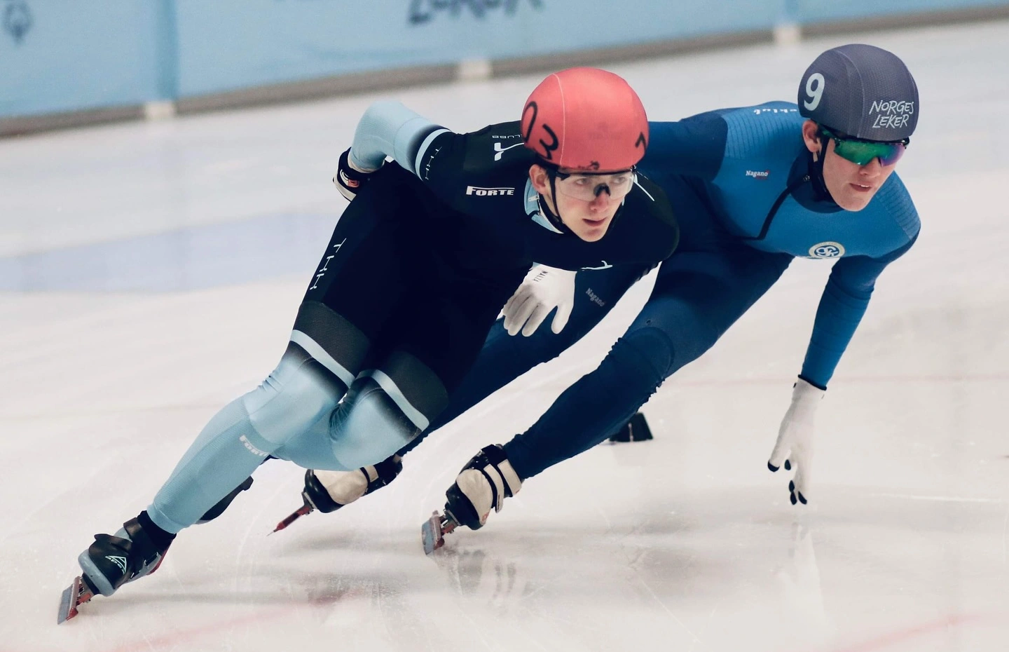 Athletes competing in a thrilling short track speed skating race, their skates carving sharp curves on the icy indoor track.