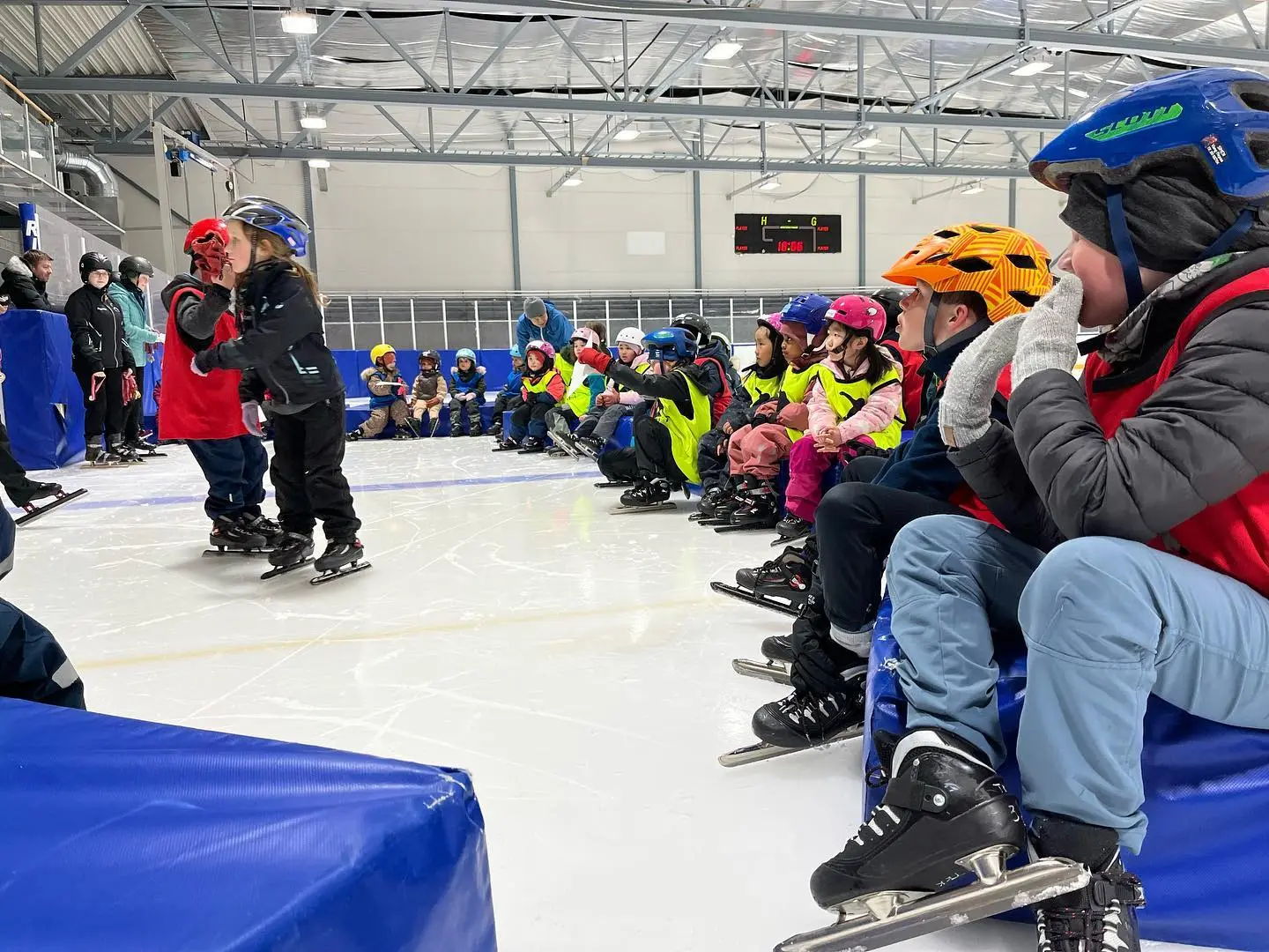 A group of short track speed skating school children resting on the rink, recovering and hydrating after a rigorous training session.